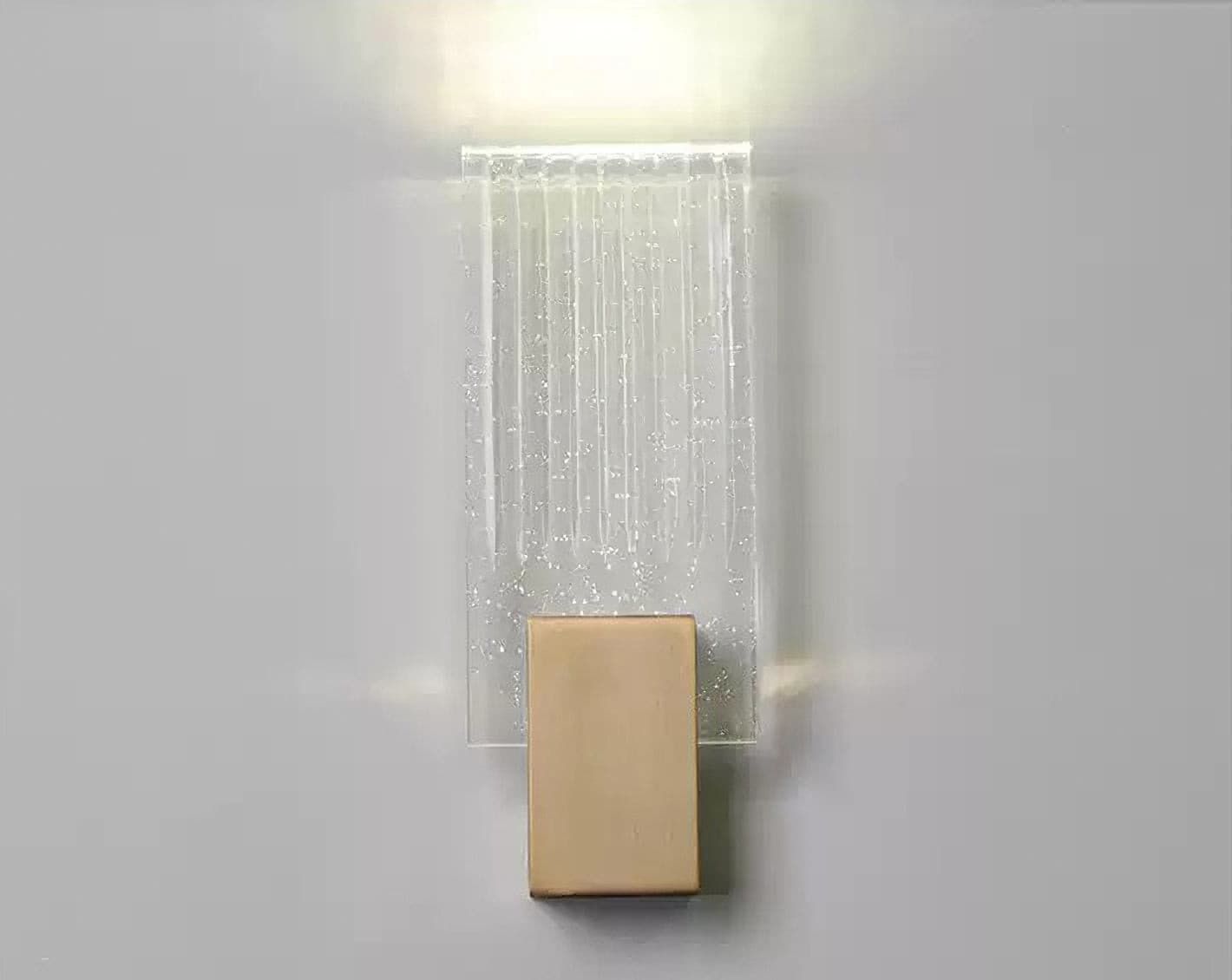 Wall light with a ribbed clear glass panel and a brushed brass mount lit, seen close against a pale wall.