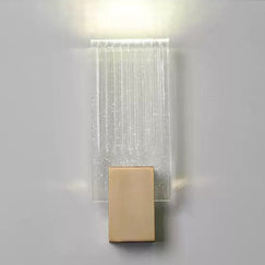 Wall light with a ribbed clear glass panel and a brushed brass mount lit, seen close against a pale wall.