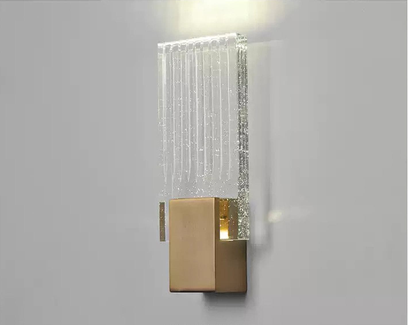 Wall light with a ribbed clear glass panel and a brushed brass mount lit against a pale wall, seen close.