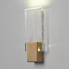 Wall light with a ribbed clear glass panel and a brushed brass mount lit against a pale wall, seen close.