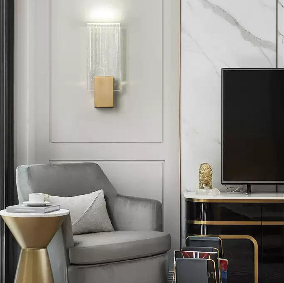 Wall light with a ribbed clear glass panel and a brushed brass mount on a panelled wall in a living room.