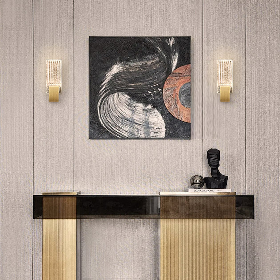 Two of the wall lights lit either side of a framed picture above a console table.