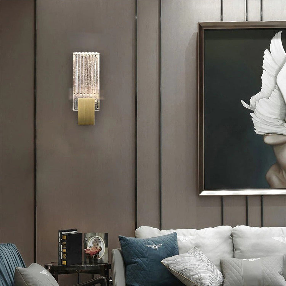 Wall light with a ribbed clear glass panel and a brushed brass mount on a panelled wall beside a framed picture.