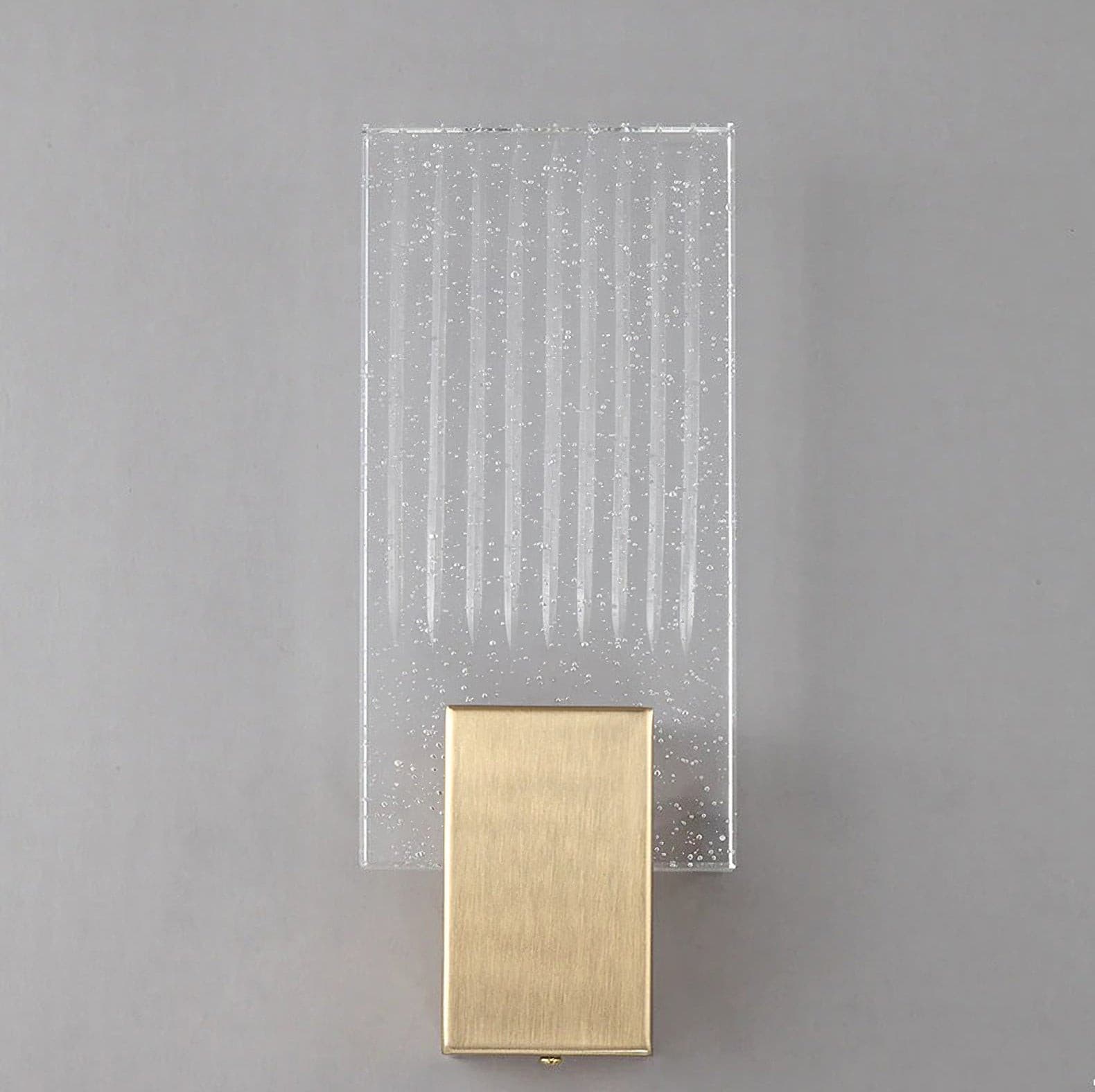 Wall light with a ribbed clear glass panel and a brushed brass mount unlit, shown close on a plain wall.