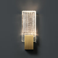 Wall light with a ribbed clear glass panel and a brushed brass mount lit against a dark grey wall.