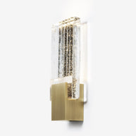 Wall light with a ribbed clear glass panel and a brushed brass mount seen at an angle, lit, on a white background.