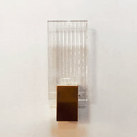 Wall light with a ribbed clear glass panel and a brushed brass mount, seen at an angle on a pale wall.