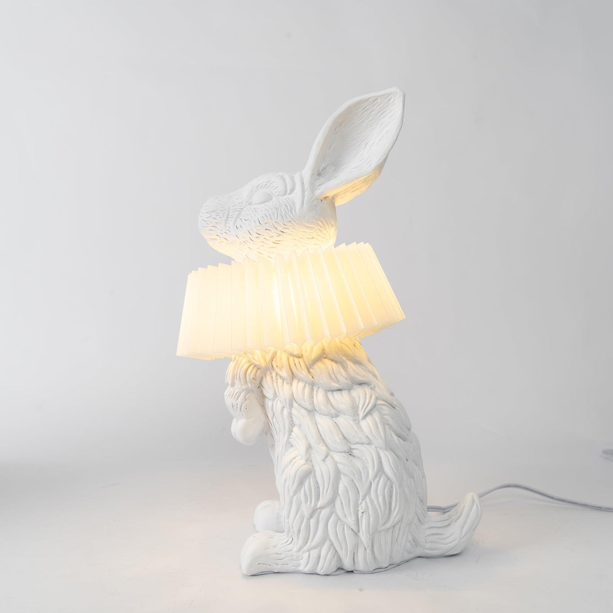 Rabellin Table Lamp - standing white leaf-textured rabbit with pleated ruff shade glowing warm on a white plinth