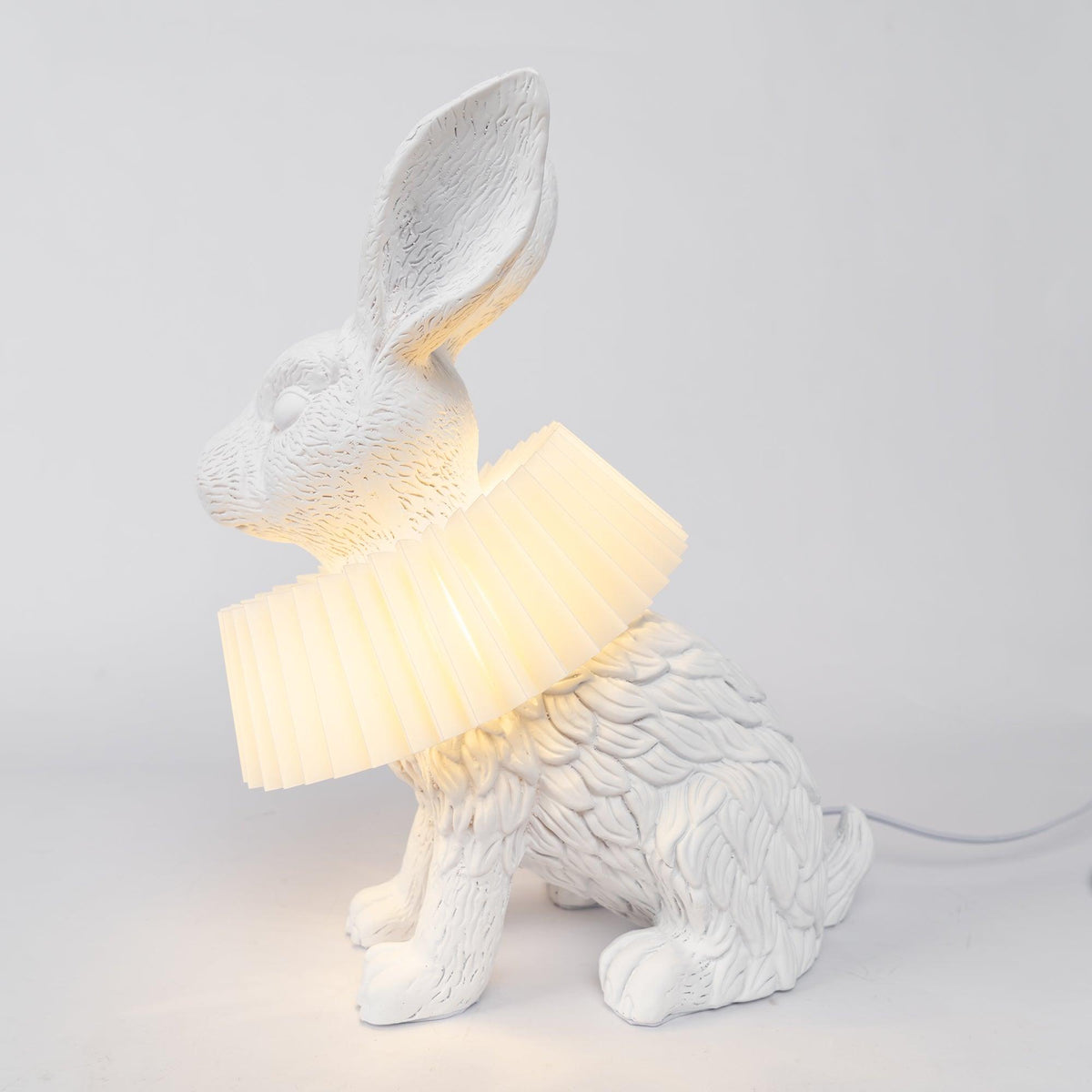 Rabellin Table Lamp - seated white leaf-textured rabbit with pleated ruff shade glowing warm on a white plinth