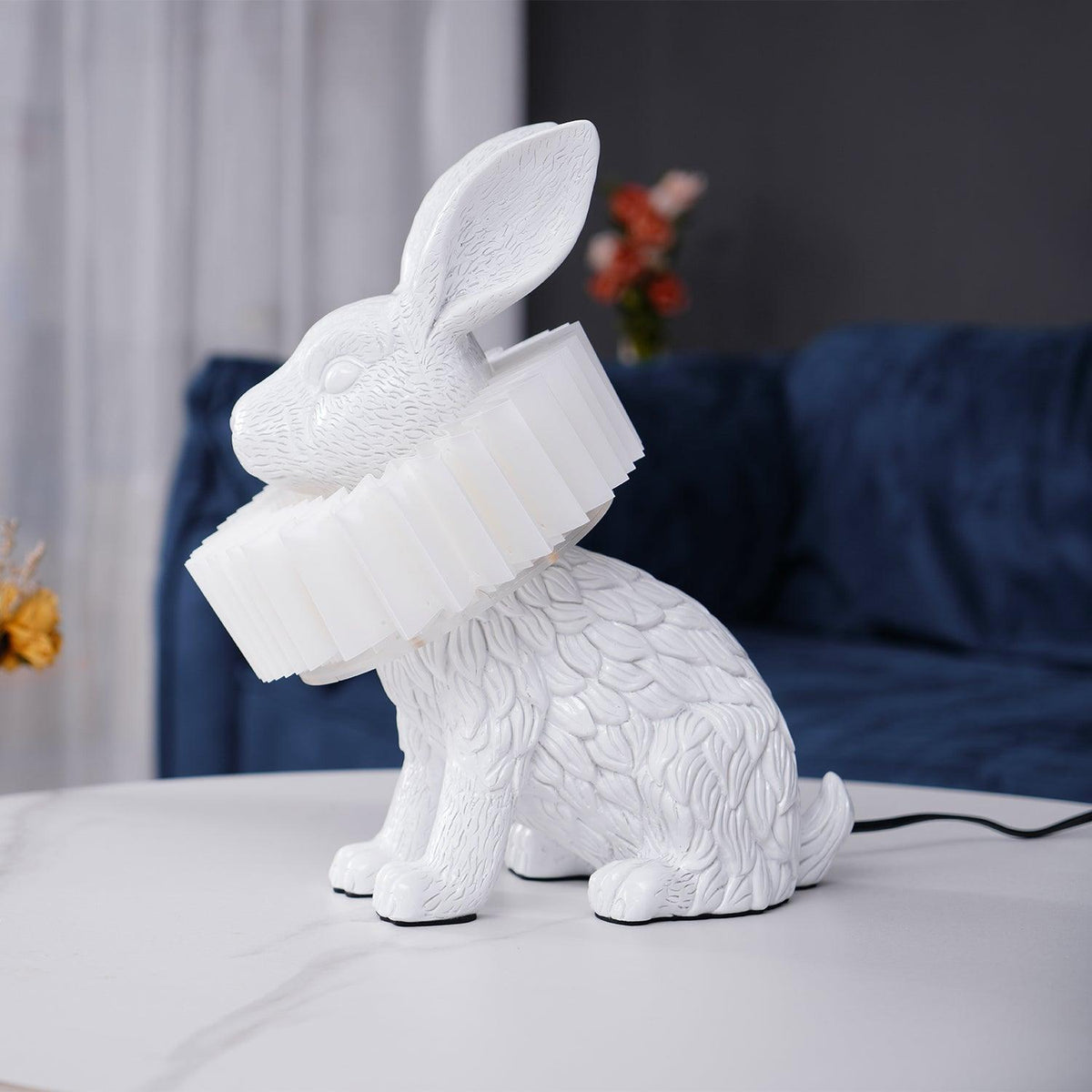 Rabellin Table Lamp - seated white leaf-textured rabbit with pleated ruff shade, unlit on a marble coffee table