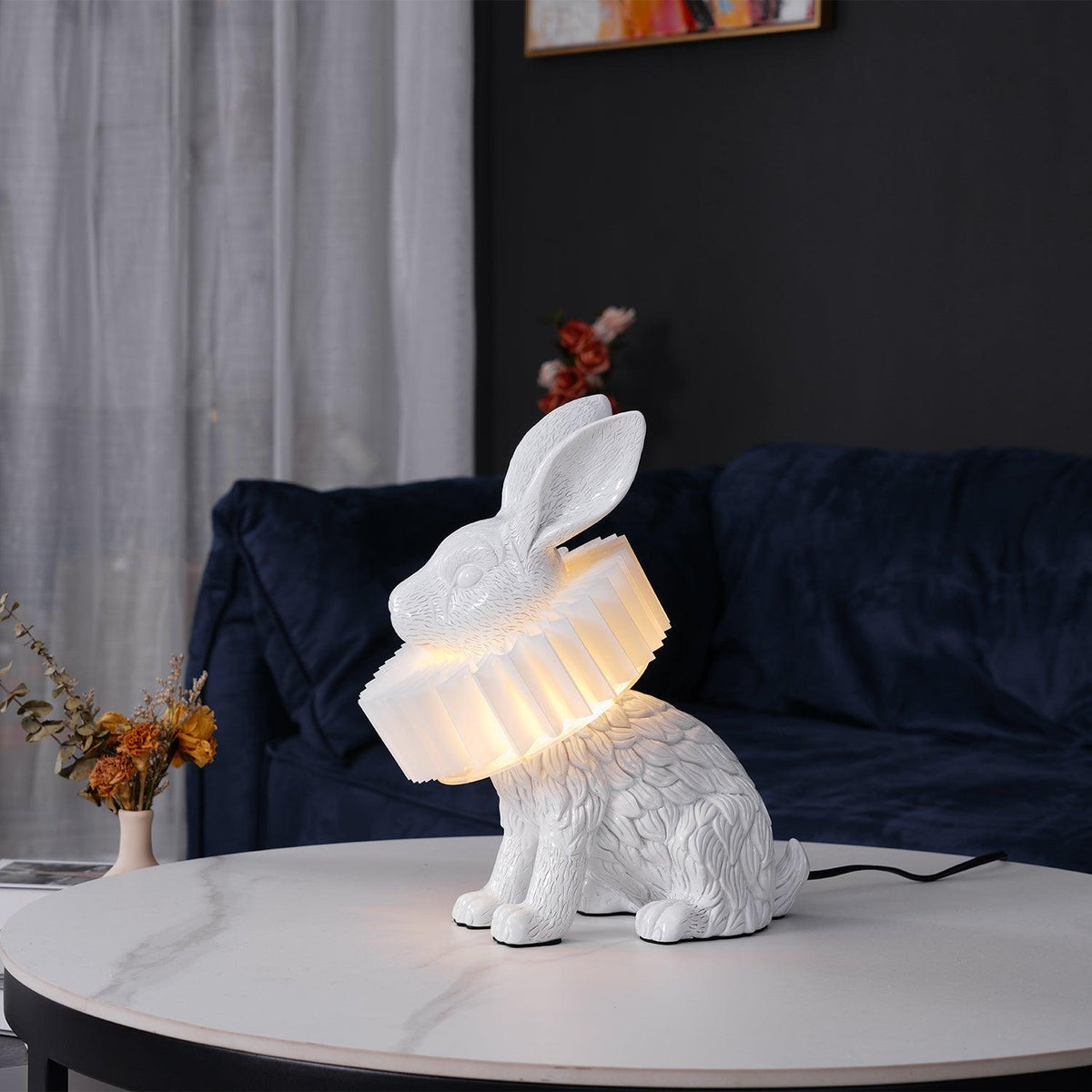Rabellin Table Lamp - seated white leaf-textured rabbit with pleated ruff shade glowing warm on a marble coffee table