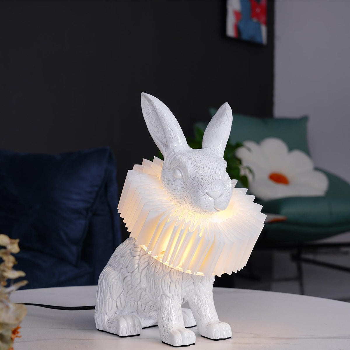 Rabellin Table Lamp - seated white leaf-textured rabbit with pleated ruff shade glowing warm on a marble coffee table