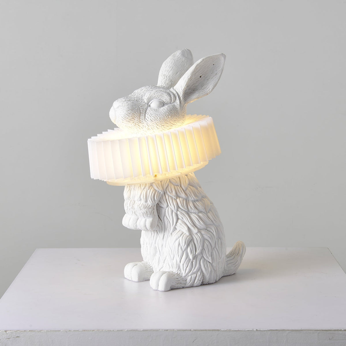 Rabellin Table Lamp - standing white leaf-textured rabbit with pleated ruff shade glowing warm on a white plinth