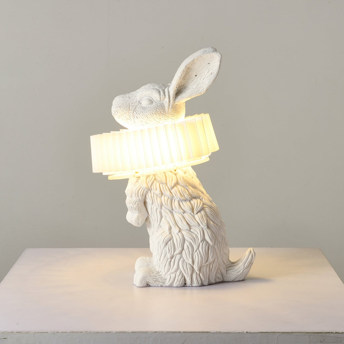 Rabellin Table Lamp - seated white leaf-textured rabbit with pleated ruff shade glowing warm on a white plinth