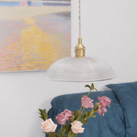 Pendant light with a ribbed glass dome shade and a gold-toned lamp holder hanging above roses, seen from a little further back.