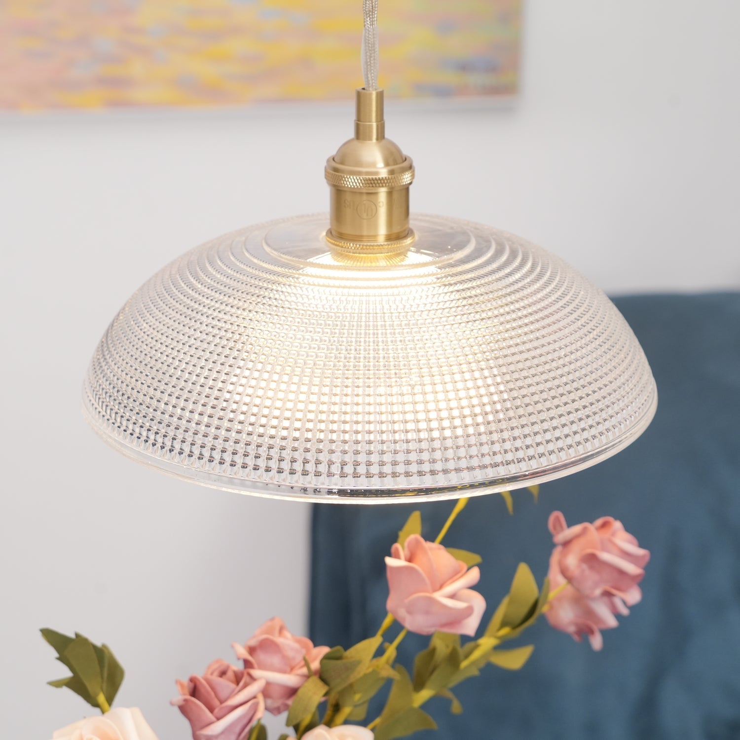Pendant light with a ribbed glass dome shade and a gold-toned lamp holder, lit, seen close above a vase of roses.