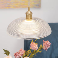 Pendant light with a ribbed glass dome shade and a gold-toned lamp holder, lit, seen close above a vase of roses.