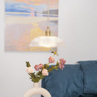 Pendant light with a ribbed glass dome shade and a gold-toned lamp holder hanging in a bedroom above roses and a rounded vase.