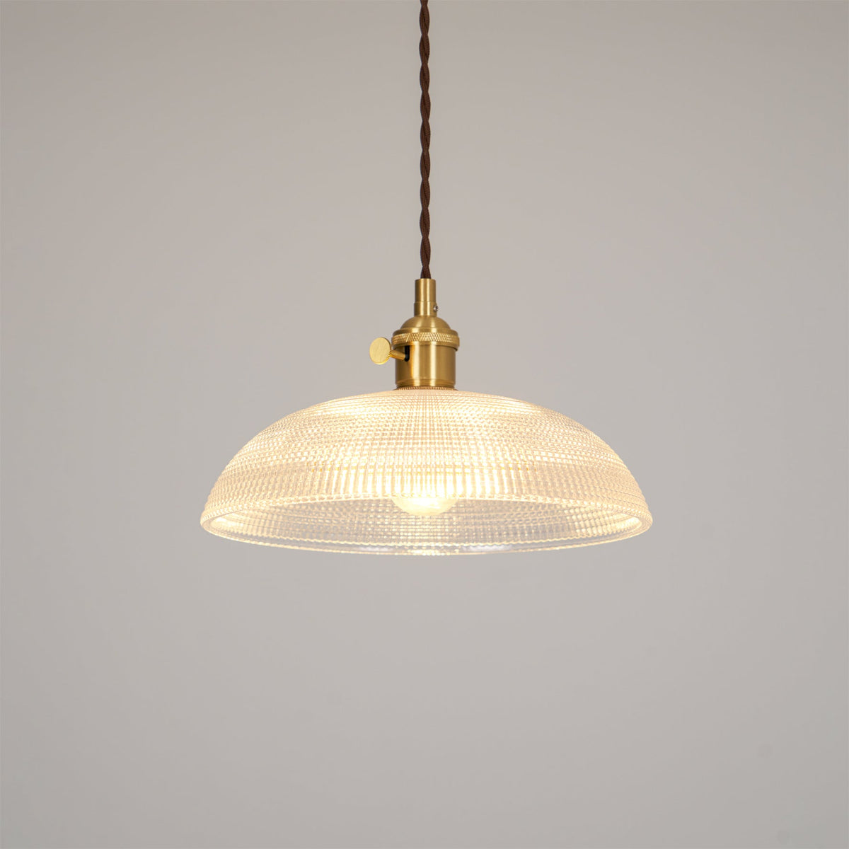 Pendant light with a ribbed glass dome shade and a gold-toned lamp holder, lit, shown on a plain pale background.
