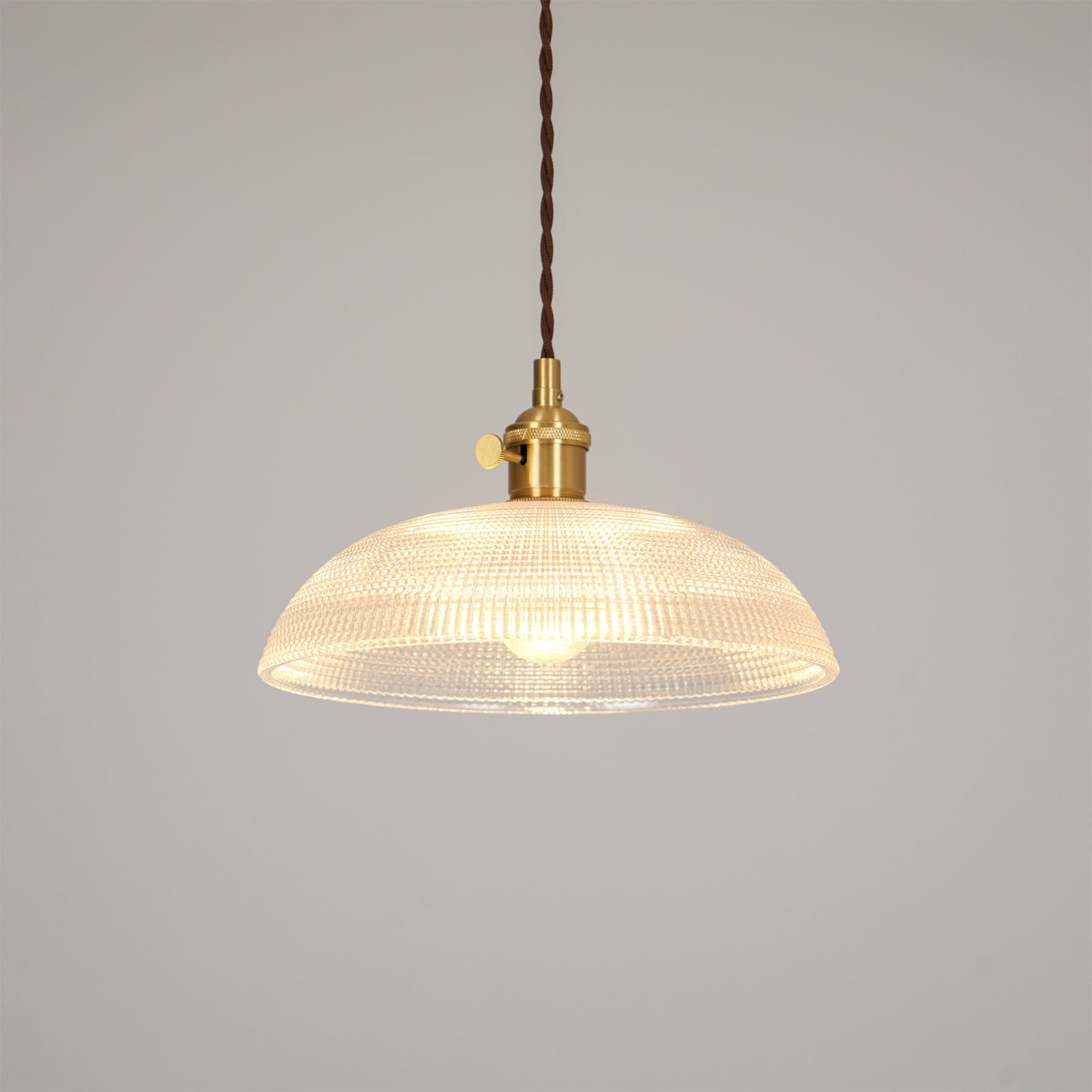 Pendant light with a ribbed glass dome shade and a gold-toned lamp holder, lit, shown on a plain pale background.