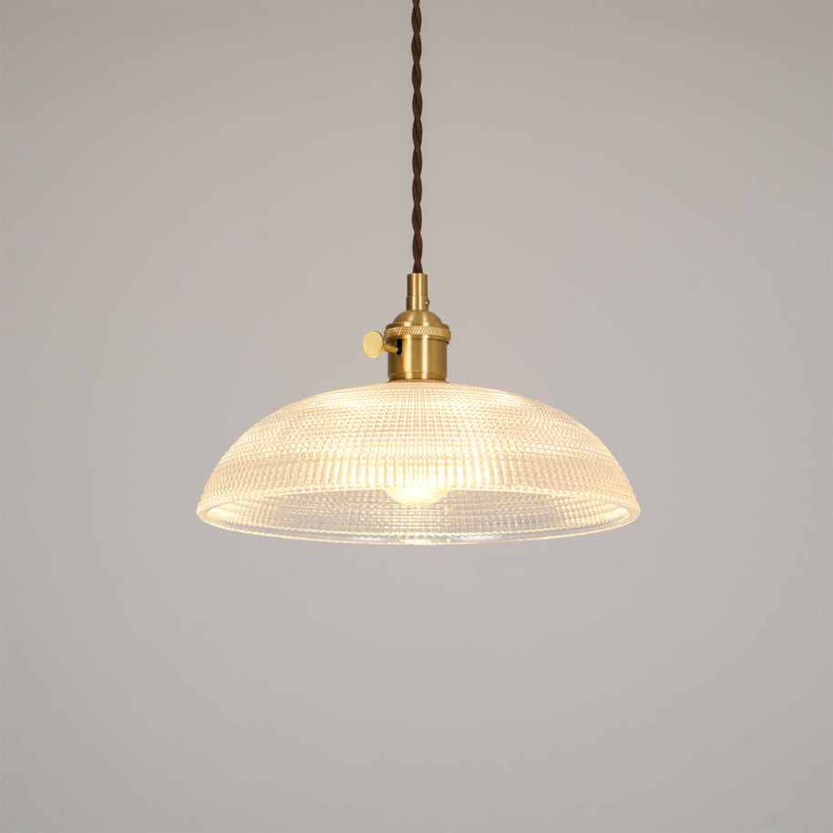 Pendant light with a ribbed glass dome shade and a gold-toned lamp holder, lit, shown on a plain pale background.