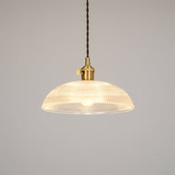 Pendant light with a ribbed glass dome shade and a gold-toned lamp holder, lit, shown on a plain pale background.