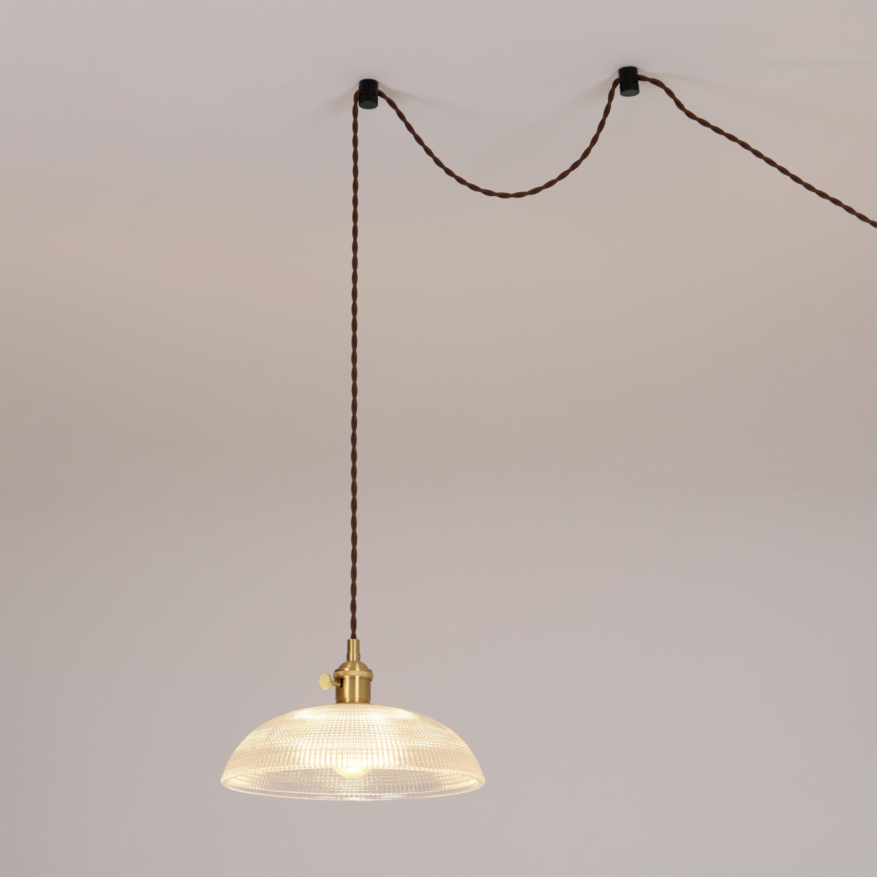 Pendant light with a ribbed glass dome shade and a gold-toned lamp holder hung on a looped cable from hooks in the ceiling.