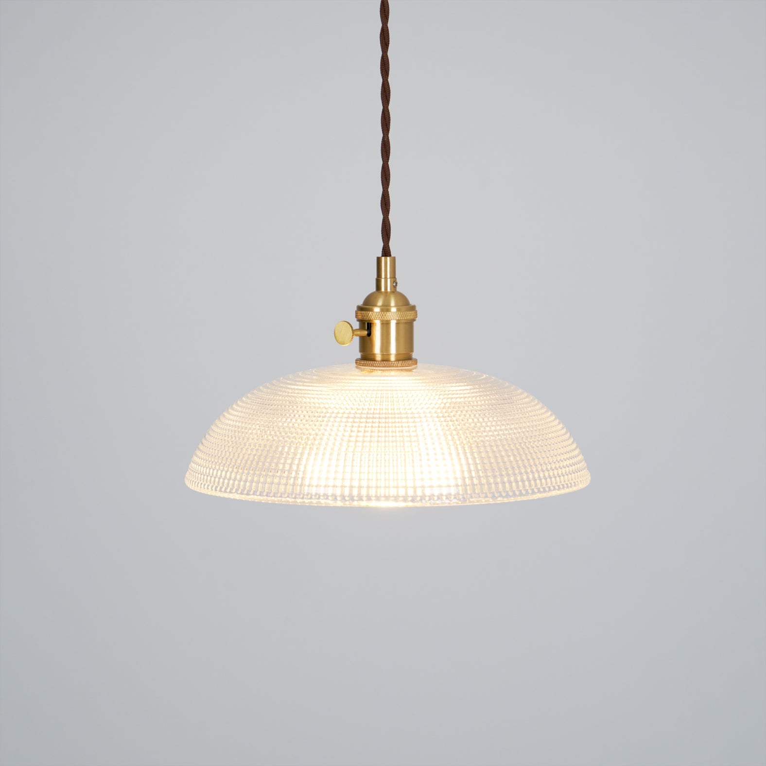 Pendant light with a ribbed glass dome shade and a gold-toned lamp holder, lit, shown on a plain grey background.