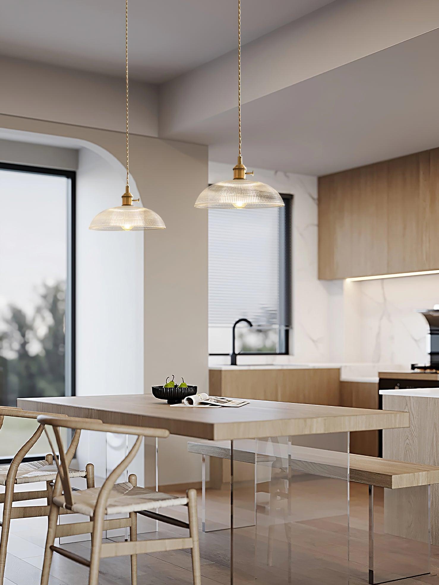 Pendant light with a ribbed glass dome shade and a gold-toned lamp holder hanging over a kitchen island in an open-plan room.