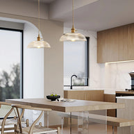 Pendant light with a ribbed glass dome shade and a gold-toned lamp holder hanging over a kitchen island in an open-plan room.