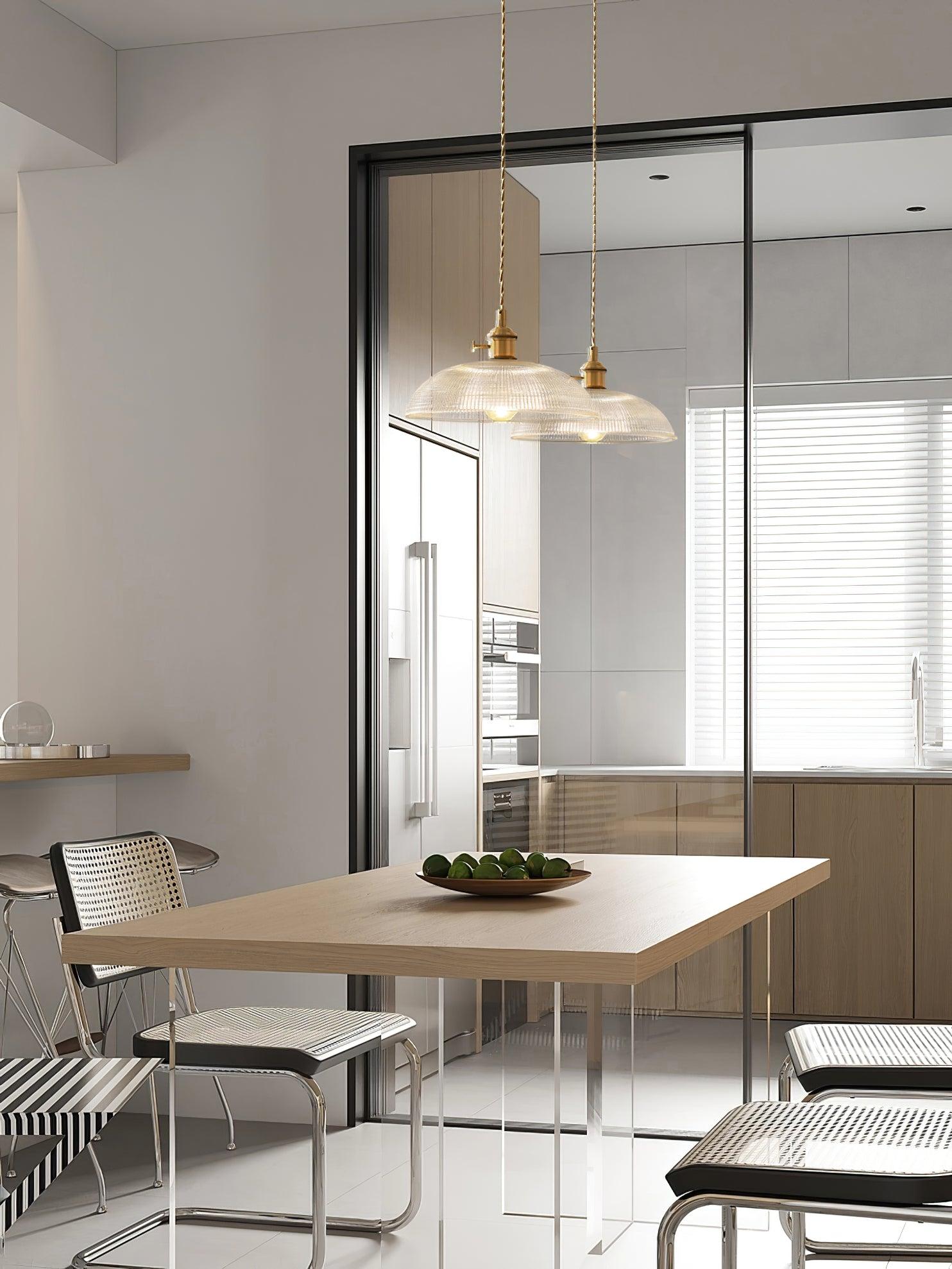 Pendant light with a ribbed glass dome shade and a gold-toned lamp holder hanging over a dining table, seen through glazing.
