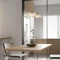 Pendant light with a ribbed glass dome shade and a gold-toned lamp holder hanging over a dining table, seen through glazing.