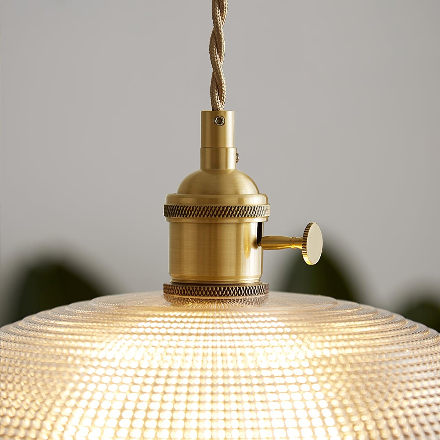Close view of the gold-toned lamp holder above the ribbed glass shade, lit.