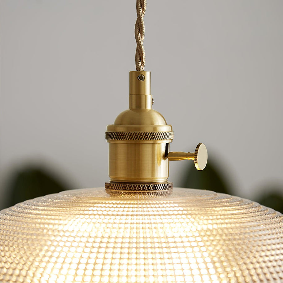 Close view of the gold-toned lamp holder above the ribbed glass shade, lit.