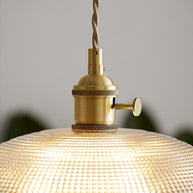 Close view of the gold-toned lamp holder above the ribbed glass shade, lit.