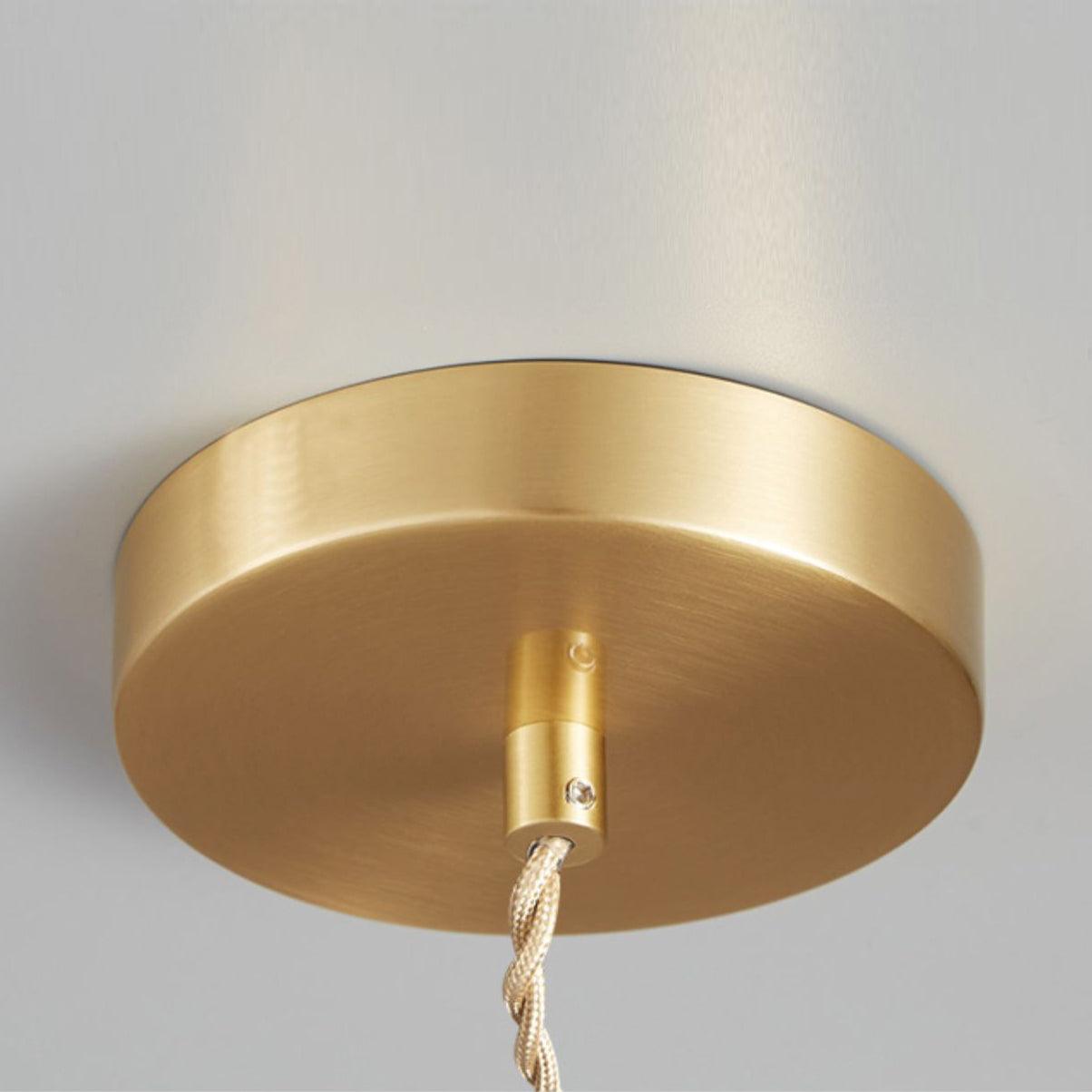 Close view of the round gold-toned ceiling plate with the twisted cable running from it.
