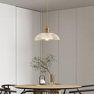 Pendant light with a ribbed glass dome shade and a gold-toned lamp holder hanging above a dining table in a pale room.