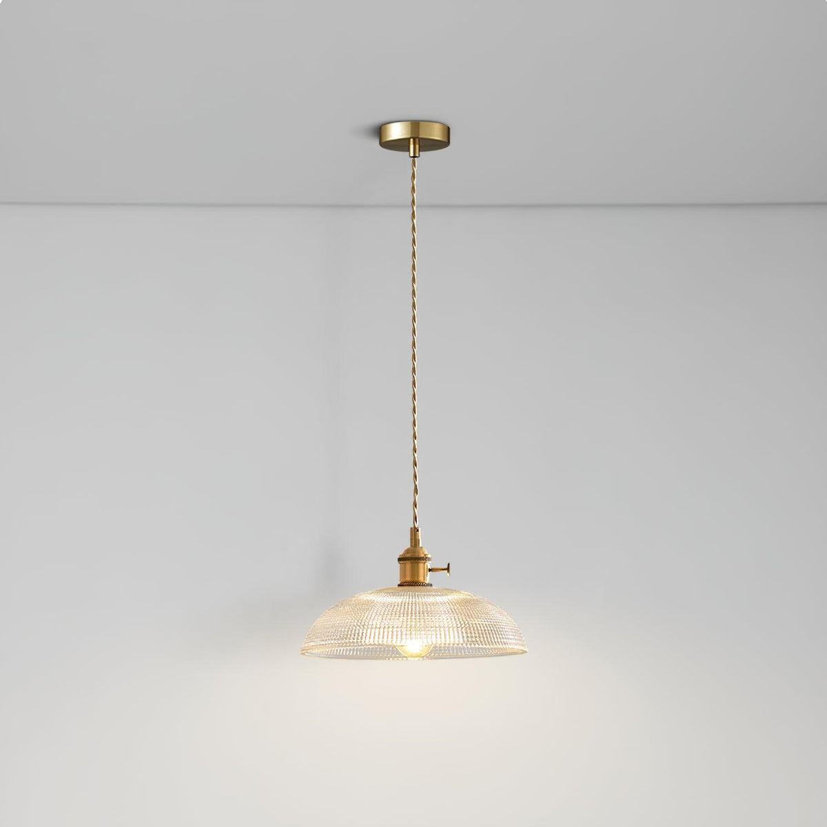 Pendant light with a ribbed glass dome shade and a gold-toned lamp holder hanging from a ceiling rose on a twisted fabric cable, lit softly.