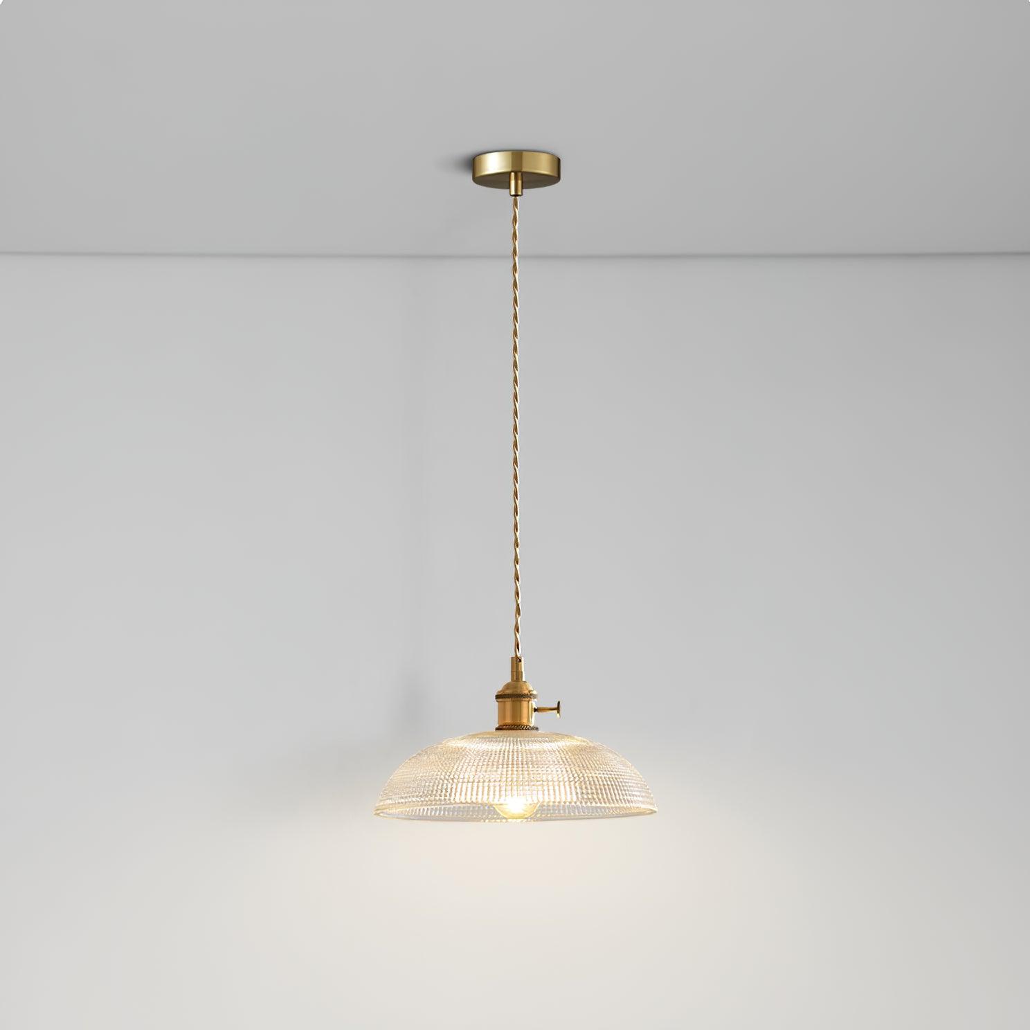 Pendant light with a ribbed glass dome shade and a gold-toned lamp holder hanging from a ceiling rose on a twisted fabric cable, lit softly.
