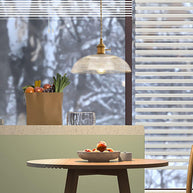 Pendant light with a ribbed glass dome shade and a gold-toned lamp holder hanging over a kitchen counter, seen through a window.