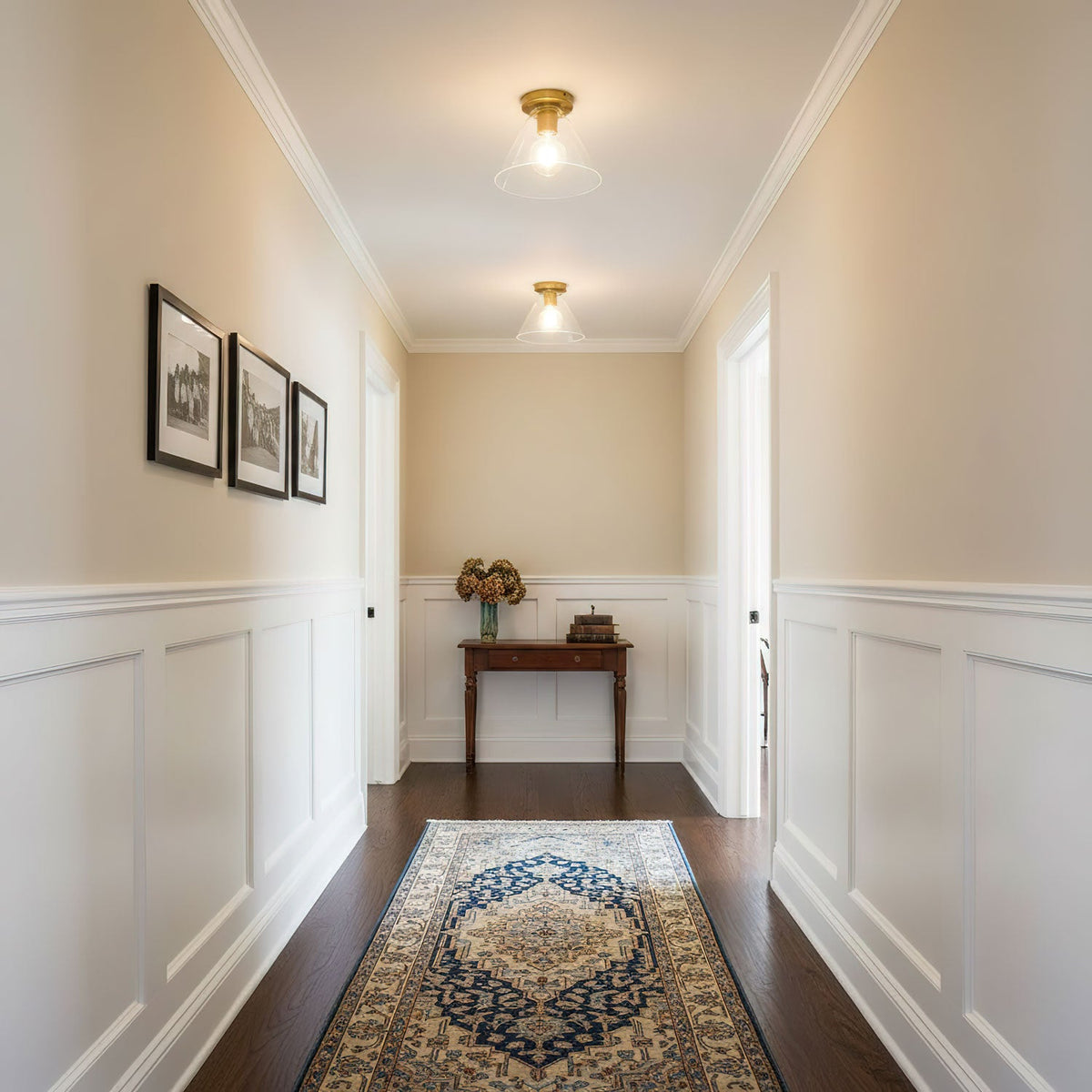 Two of the ceiling lights lit along a hallway with cream walls and white panelling.