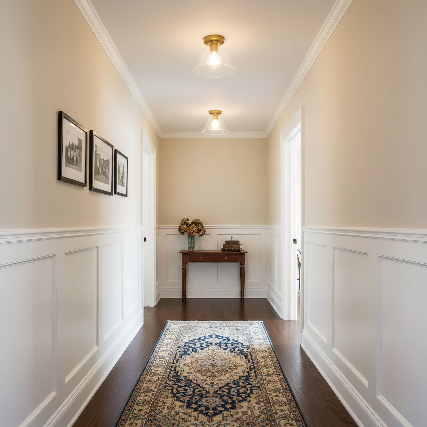 Two of the ceiling lights lit along a hallway with cream walls and white panelling.