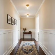 Two of the ceiling lights lit along a hallway with cream walls and white panelling.
