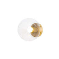Light fitting with a round brass-toned back plate and a rounded glass shade and an exposed bulb, lit, shown on a white background.