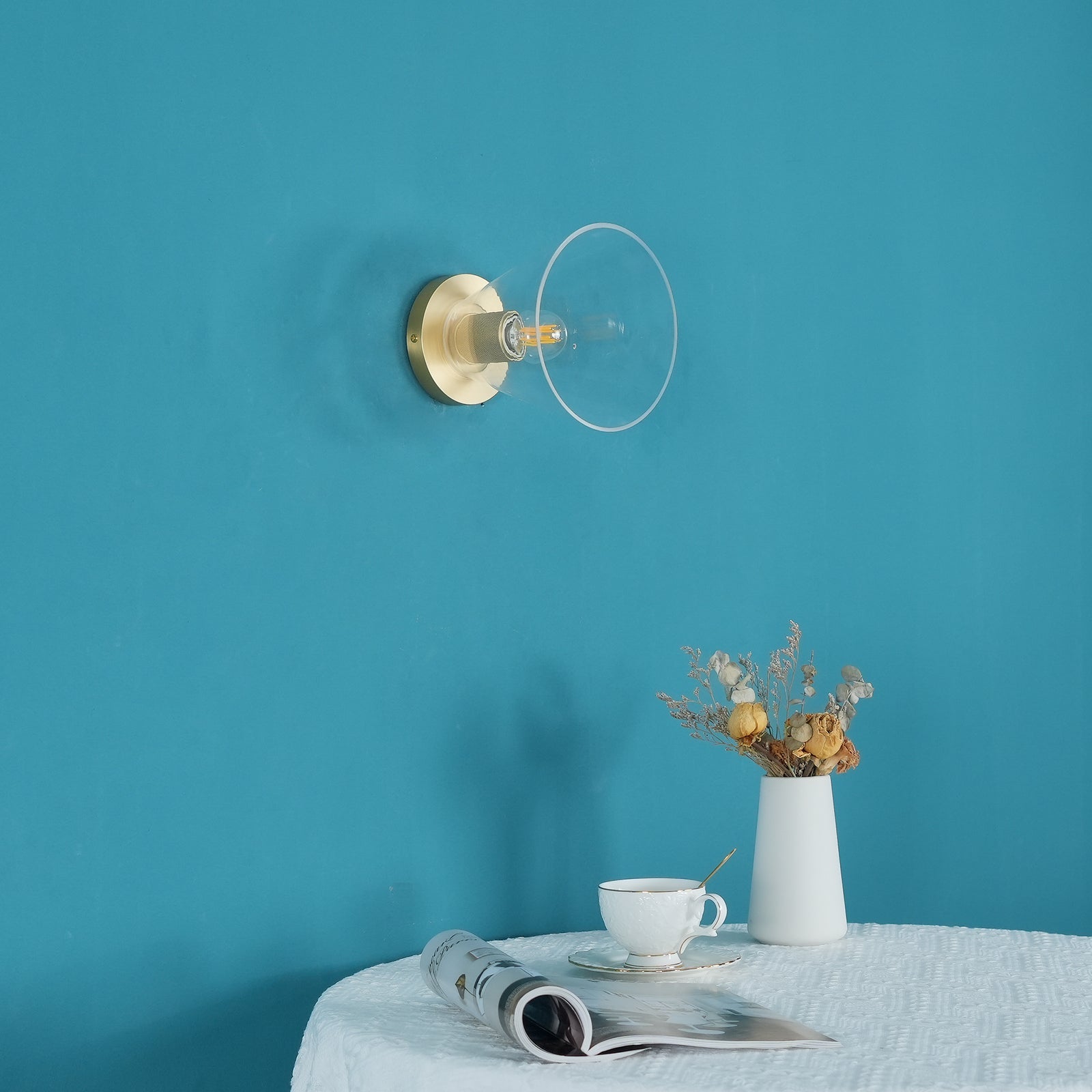 Light fitting with a round brass-toned back plate and a rounded glass shade, unlit, against a teal background.