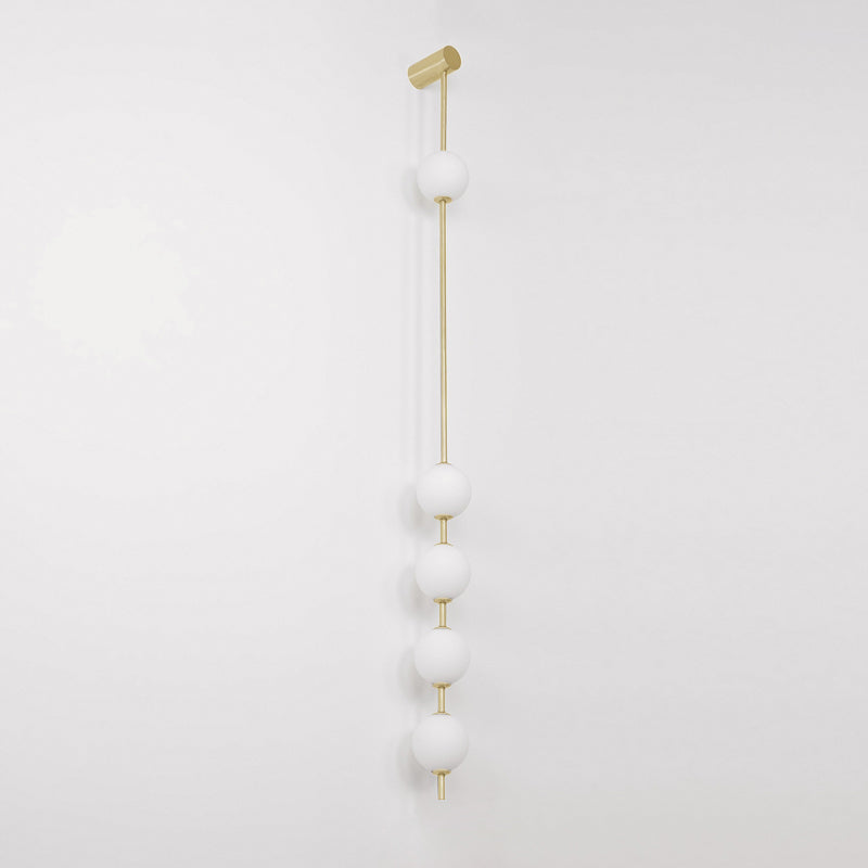 Wall lamp with a vertical row of white ball shades on a slim gold-toned rod, unlit, on a pale wall.