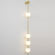Wall lamp with a vertical row of white ball shades on a slim gold-toned rod, lit, on a grey wall.