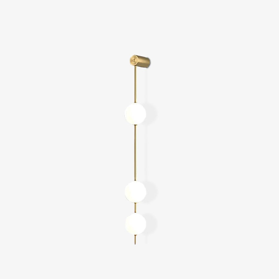 Wall lamp with a vertical row of white ball shades on a slim brass-coloured rod, unlit, on a white background.
