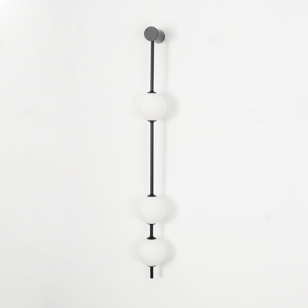 Wall lamp with a vertical row of white ball shades on a slim dark rod, unlit, on a white background.