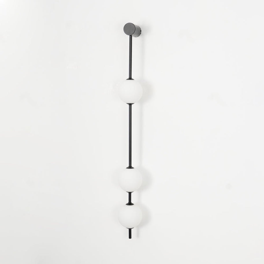 Wall lamp with a vertical row of white ball shades on a slim dark rod, unlit, on a white background.